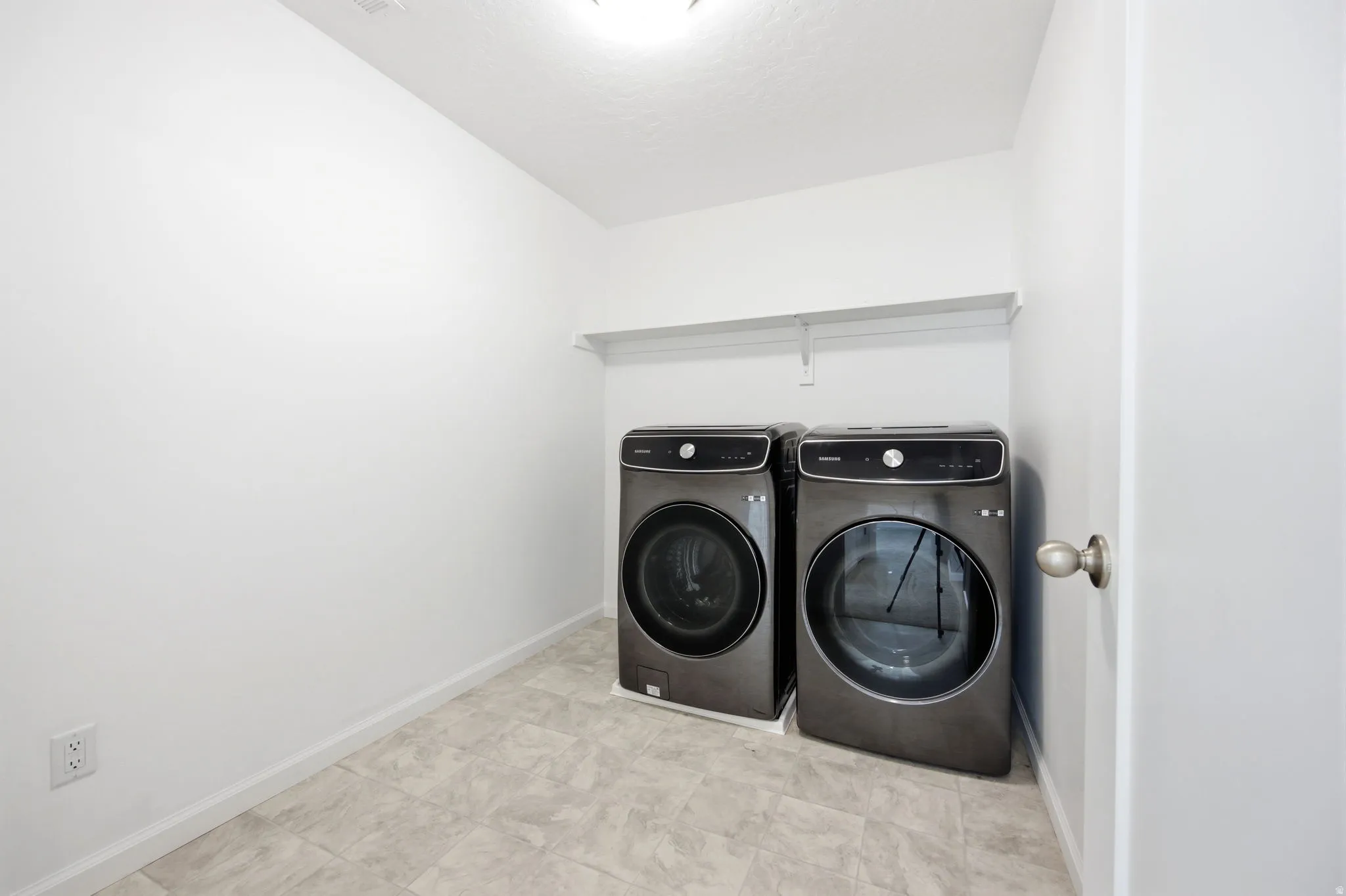 Utility area featuring a floating white shelf, light-toned flooring, and neutral wall finishes