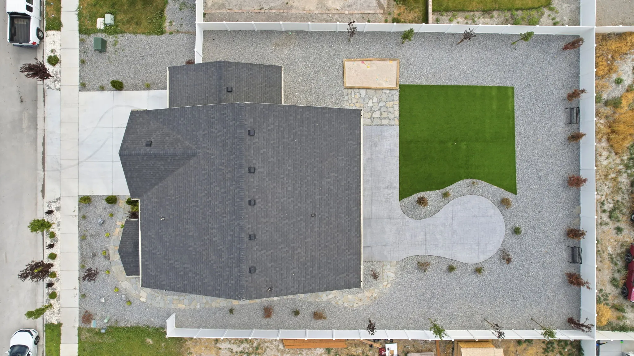 Expansive backyard featuring a rectangular artificial turf lawn, a curved concrete patio, and gravel landscaping