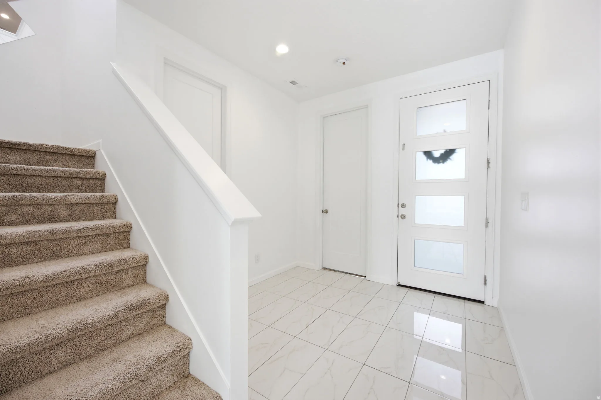 Foyer featuring white tile flooring, a modern entry door with frosted glass panels, and a carpeted staircase with a white railing