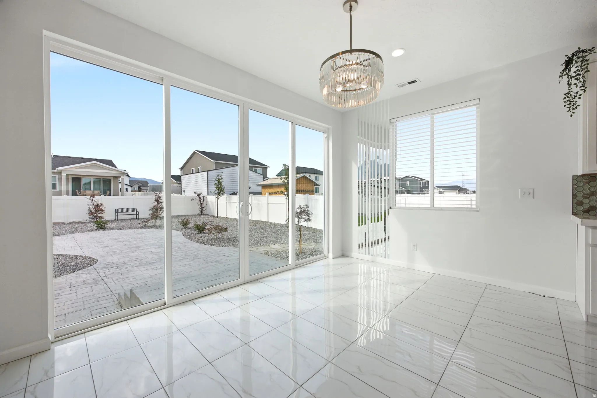 Spacious dining area featuring large sliding glass doors, white tile flooring, a contemporary chandelier, a window with blinds, and white painted walls