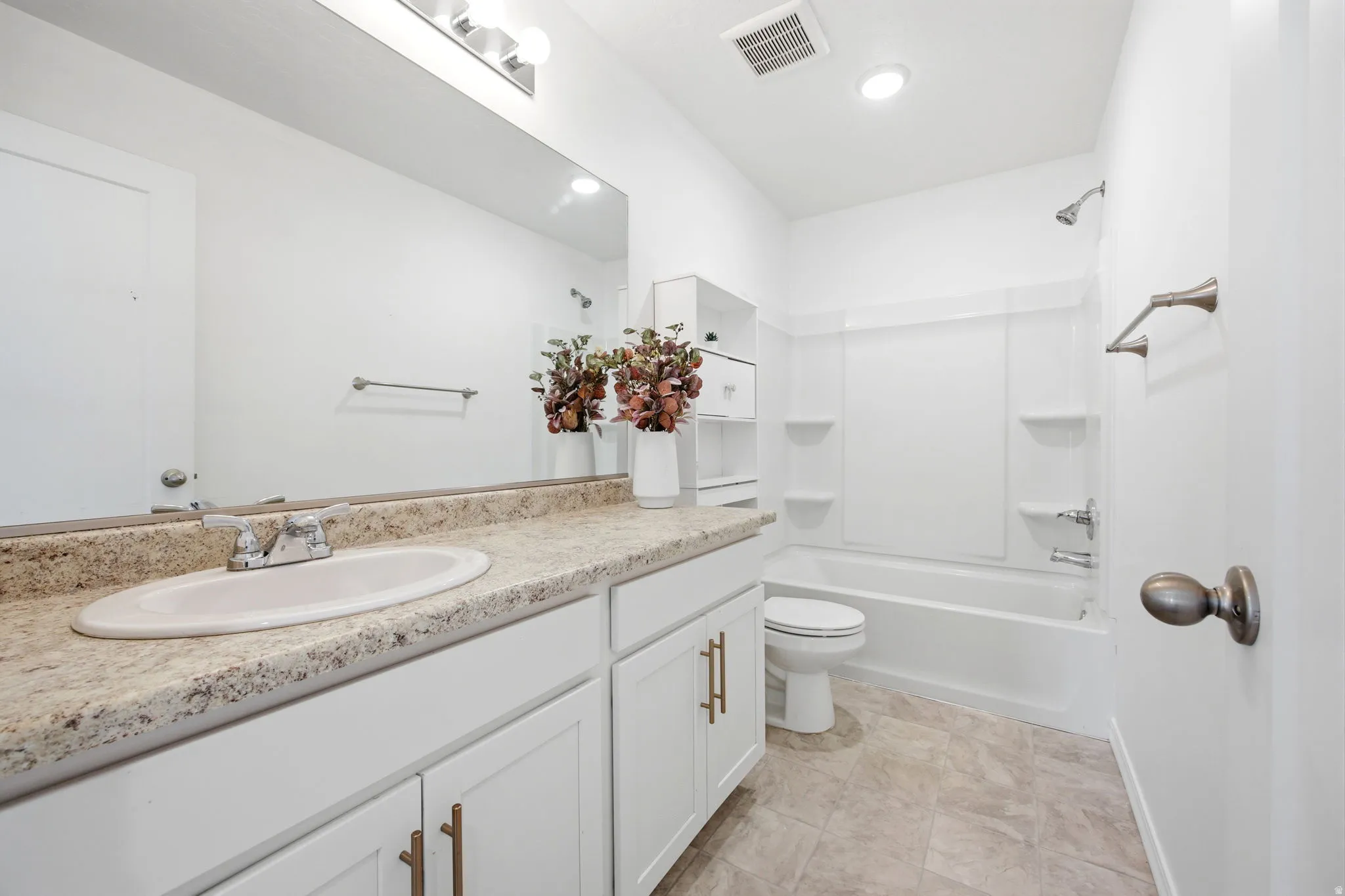 Bathroom featuring a white vanity with gold-finish hardware, an integrated sink, a speckled countertop, and a wide wall mirror