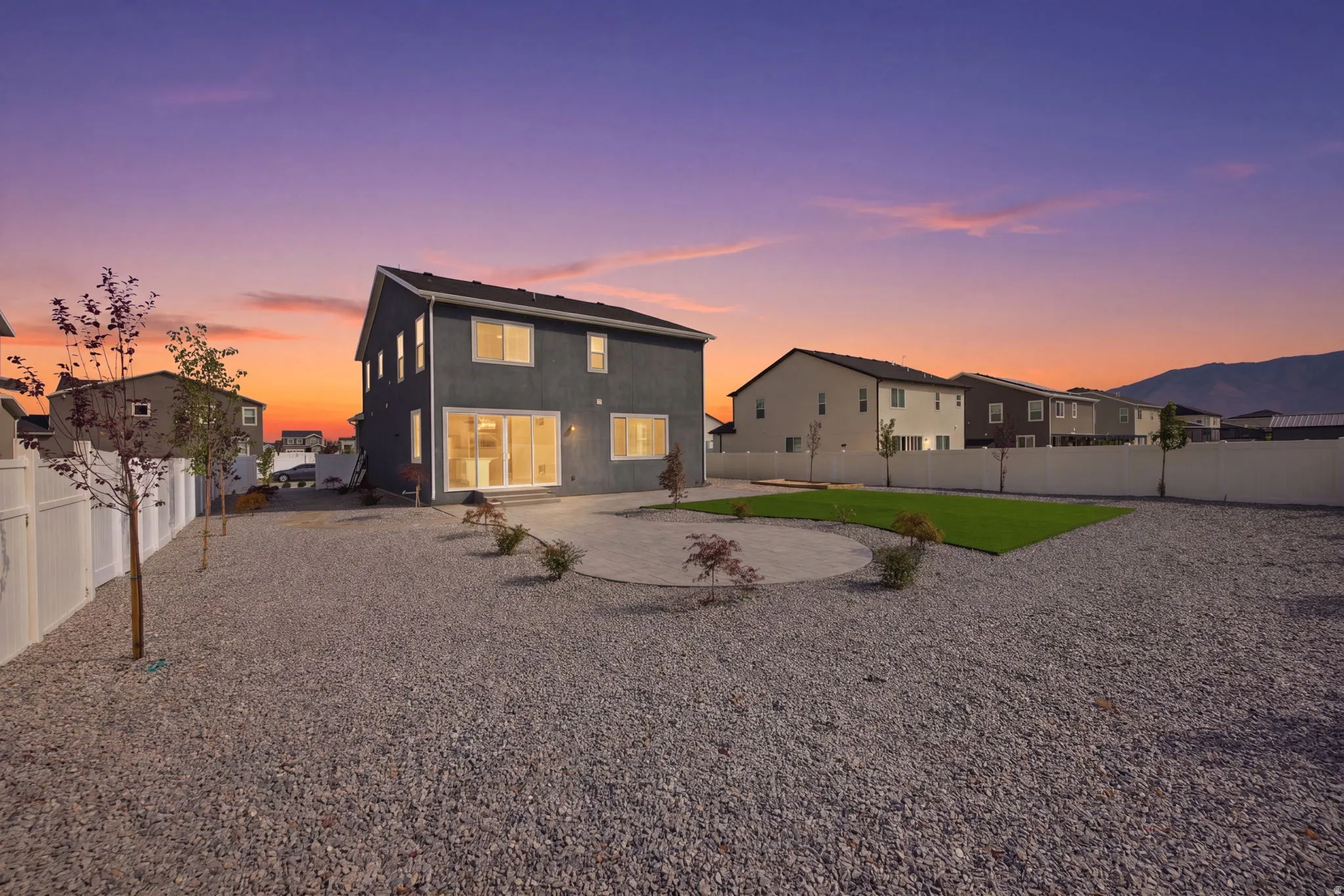 Expansive rear yard featuring a gravel landscape, a circular patio, a rectangular artificial turf area, and a white privacy fence