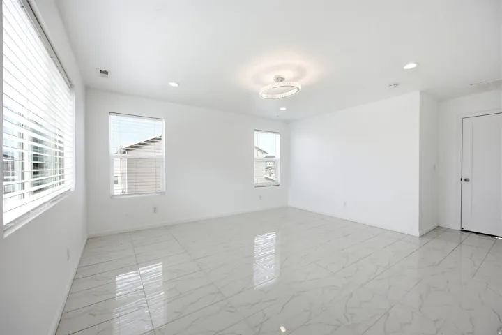 Spacious room featuring large format tile flooring, crisp white walls, and multiple windows with white blinds