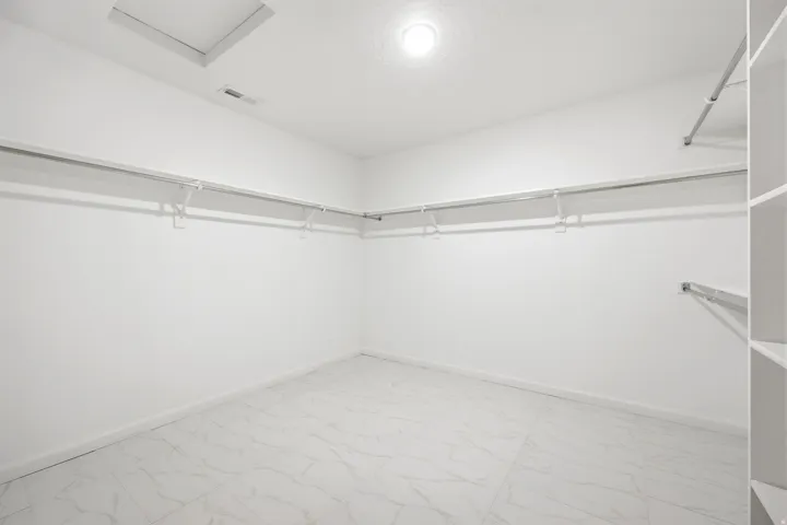 Spacious closet featuring white walls, white-finish shelving, metal hanging rods, and large format white tile flooring