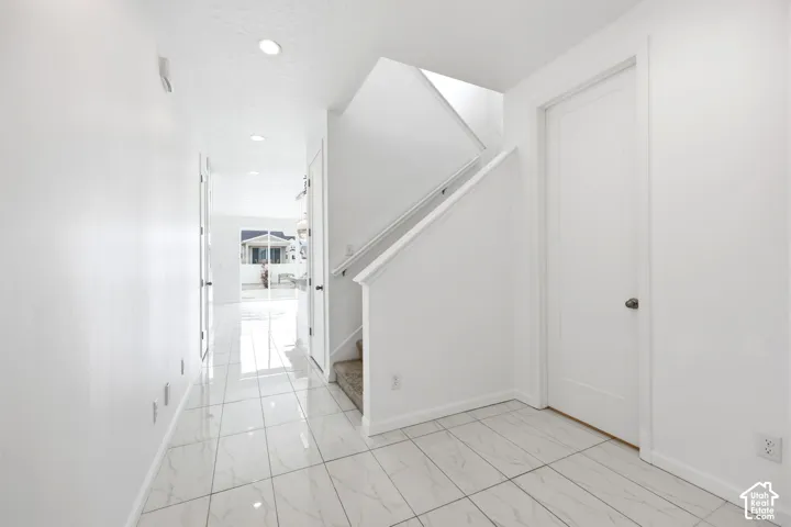 Entryway featuring large format marble-look tile flooring, white walls, recessed lighting, and a staircase with white railing