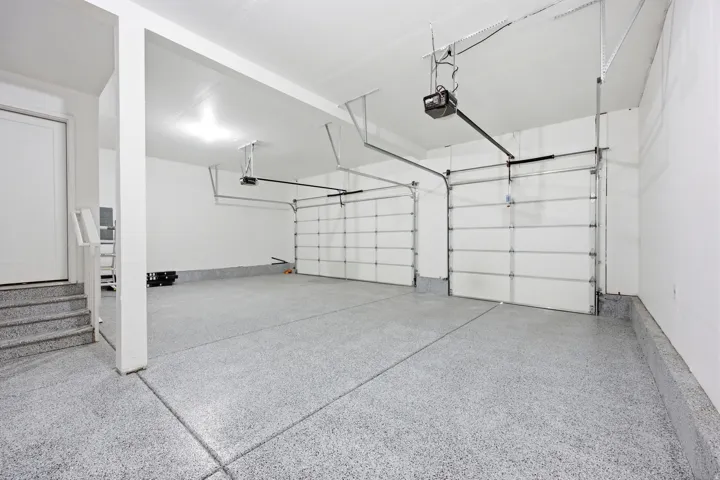 Two-car garage featuring a speckled epoxy floor coating, two overhead garage doors with automatic openers, and direct interior access via a white door and steps