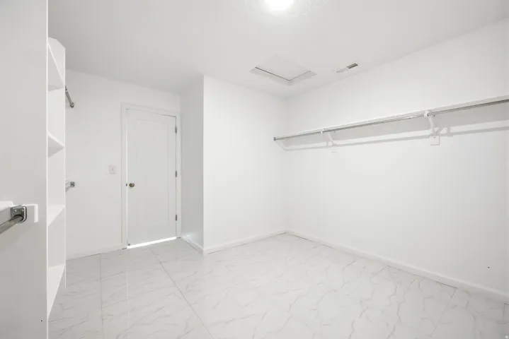 Spacious walk-in closet featuring white walls, white-finish built-in shelving, and white-finish hanging rods