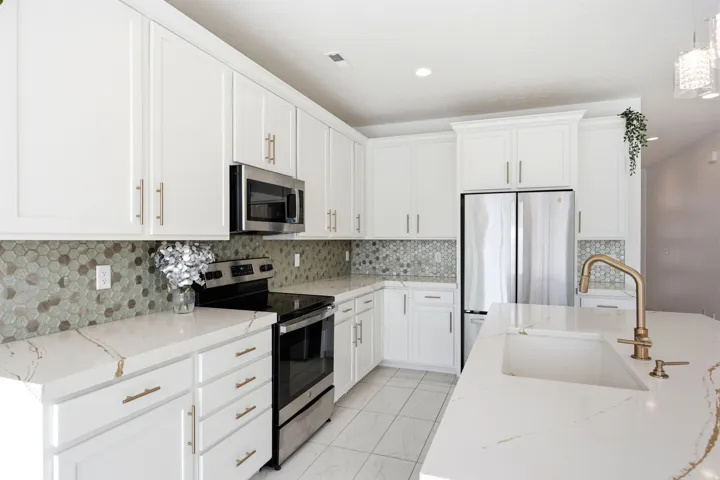 Contemporary kitchen featuring white cabinetry with gold-finish hardware, stainless steel appliances, and a hexagonal tile backsplash