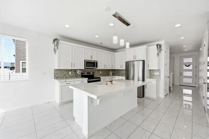 Modern kitchen featuring white shaker cabinetry, stainless steel appliances, a center island with a waterfall countertop, mosaic tile backsplash, and large format tile flooring