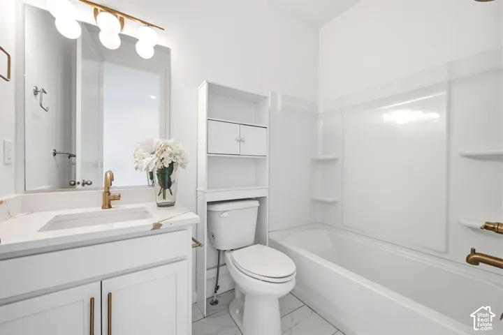 Full bathroom featuring a white vanity with a gold-tone faucet, a mirror with a spherical light fixture, a toilet with an over-the-toilet storage unit, a built-in bathtub with a white surround, and white tile flooring
