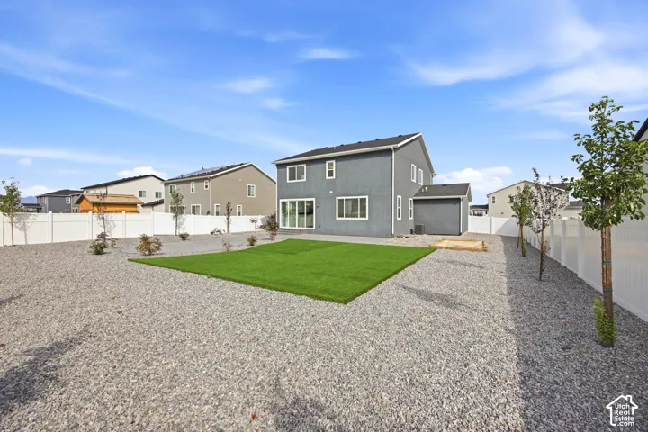 Expansive backyard featuring a central artificial turf area, surrounding gravel landscaping, a white privacy fence, and scattered young trees