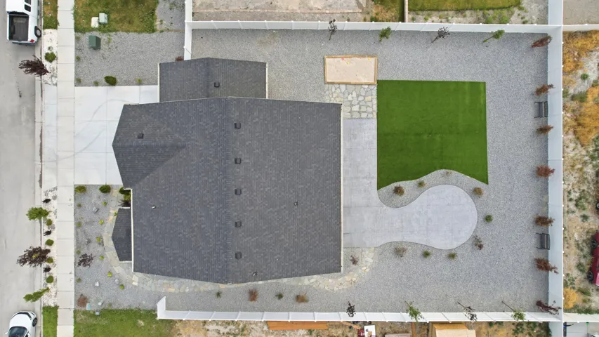Expansive backyard featuring a rectangular artificial turf lawn, a curved concrete patio, and gravel landscaping