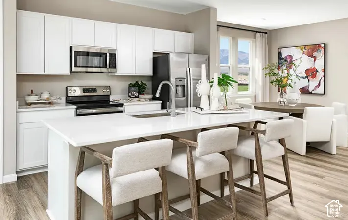 Open-concept kitchen featuring an island with counter seating, stainless steel appliances, white cabinetry, and light wood-finish flooring