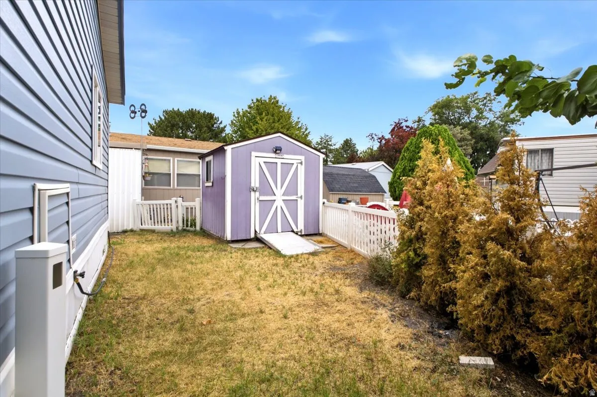 Storage shed with ramp access, complemented by a white picket fence and established shrubbery