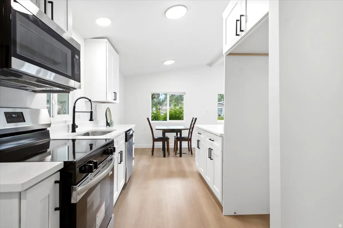 Modern kitchen featuring white shaker cabinetry, stainless steel appliances, quartz countertops, and wood-finish flooring