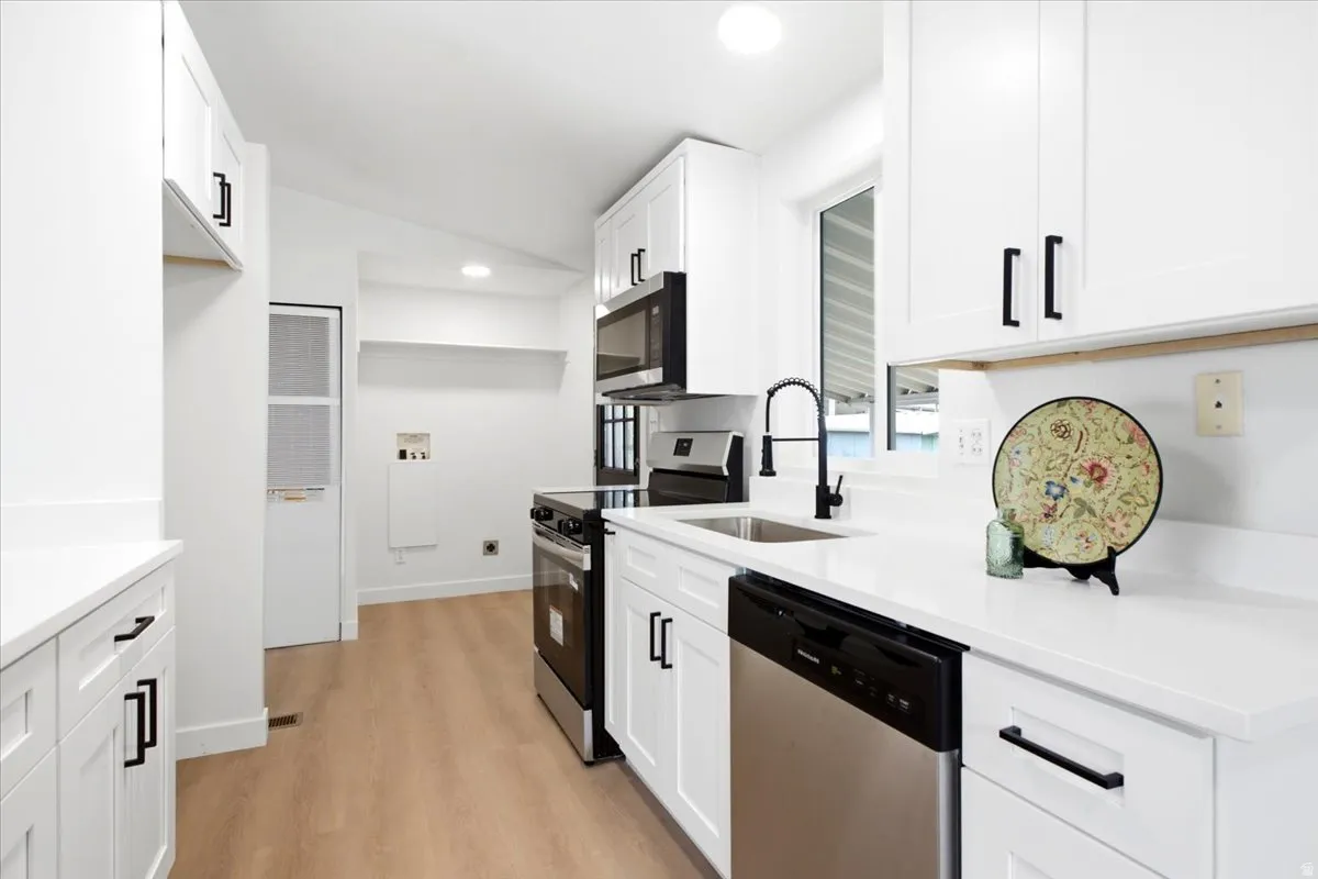Modern kitchen featuring white cabinetry, stainless steel appliances, light wood-finish flooring, a matte black faucet, and a large window
