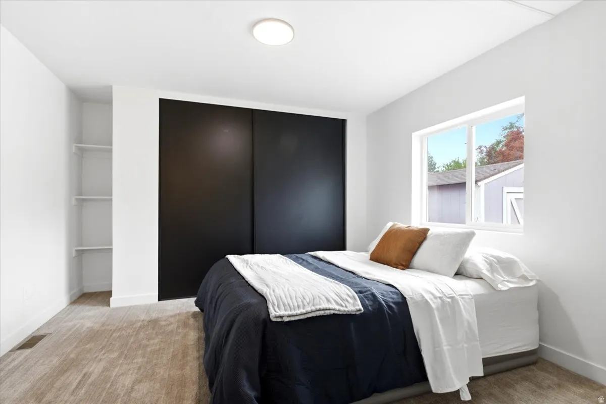 Bedroom featuring light neutral carpeting, a window, built-in shelving, a flush-mount ceiling light, and a two-panel sliding closet door
