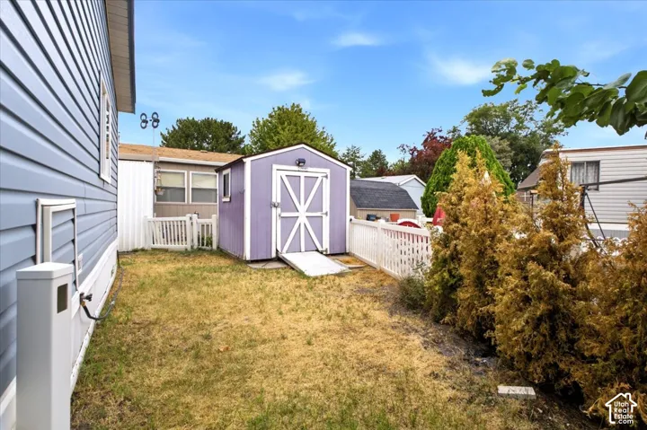 Storage shed with ramp access, complemented by a white picket fence and established shrubbery