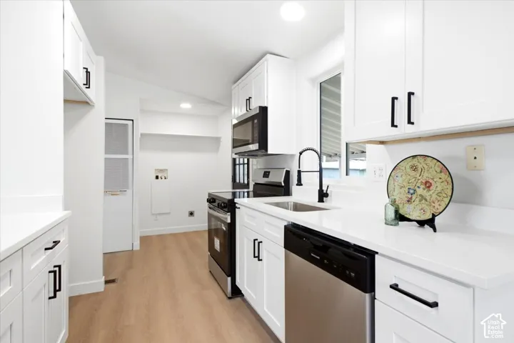 Modern kitchen featuring white cabinetry, stainless steel appliances, light wood-finish flooring, a matte black faucet, and a large window