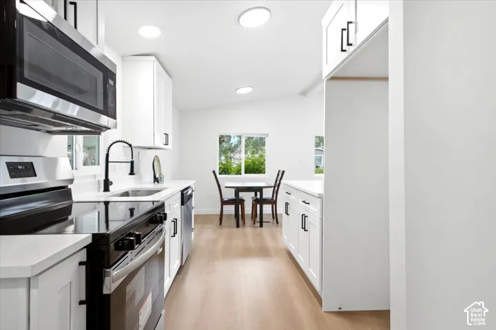 Modern kitchen featuring white shaker cabinetry, stainless steel appliances, quartz countertops, and wood-finish flooring