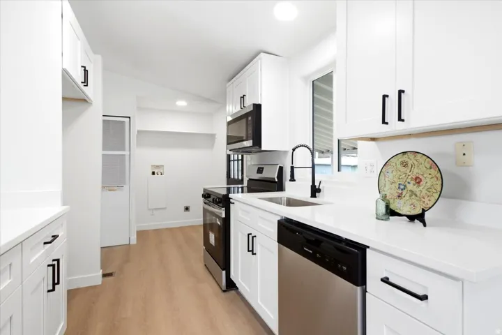 Modern kitchen featuring white cabinetry, stainless steel appliances, light wood-finish flooring, a matte black faucet, and a large window