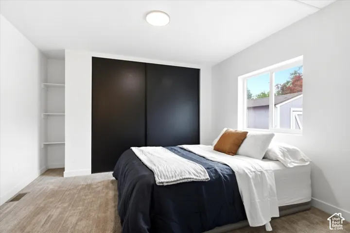 Bedroom featuring light neutral carpeting, a window, built-in shelving, a flush-mount ceiling light, and a two-panel sliding closet door
