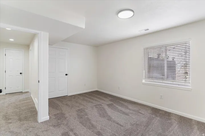 Spacious room featuring gray patterned carpeting, a single window with blinds, and a flush-mount ceiling light