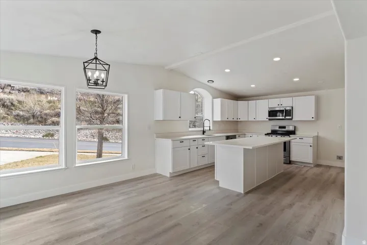 Open-concept kitchen and dining area featuring light wood-finish flooring, white cabinetry, a central island, stainless steel appliances, and a modern black chandelier