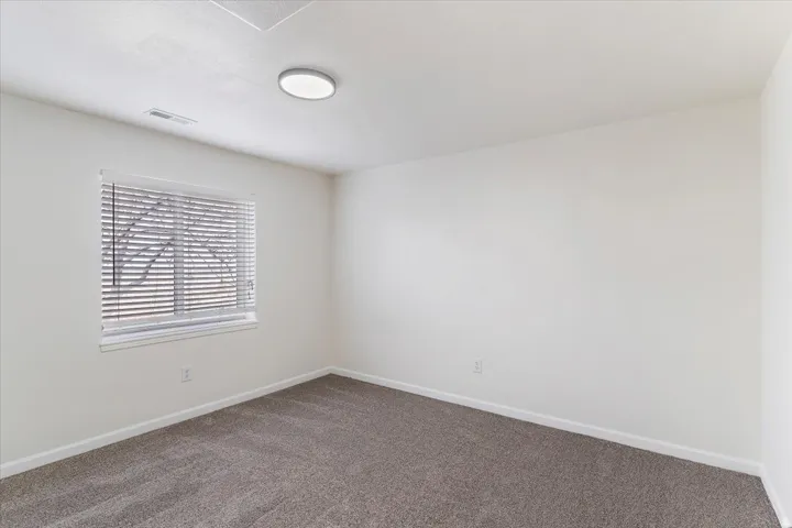 Carpeted room featuring a single window with horizontal blinds, a flush-mount ceiling light fixture, and white wall finishes