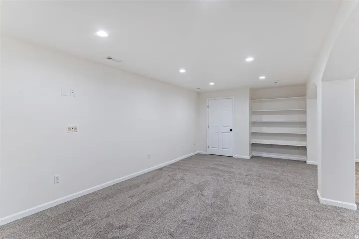 Spacious room featuring neutral carpeting, recessed lighting, built-in shelving, a paneled door, and an arched entryway