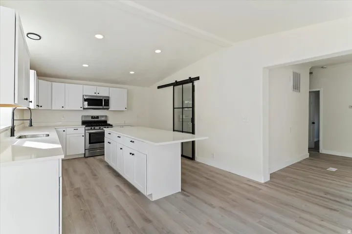 Kitchen featuring white shaker cabinetry, stainless steel appliances, light-toned countertops, and wood-finish flooring