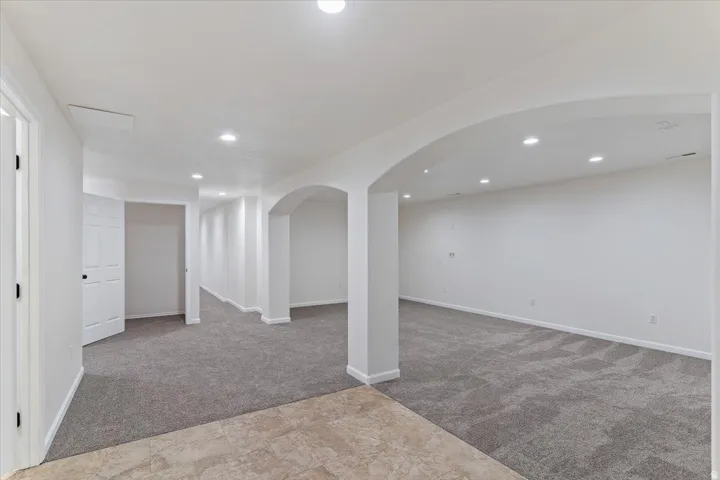 Spacious interior featuring neutral carpeting, arched doorways, white walls, recessed lighting, and a neutral tile floor entrance