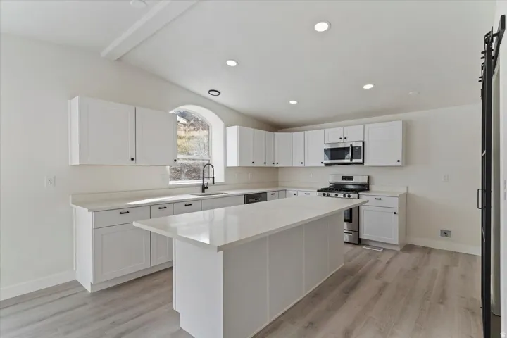Contemporary kitchen featuring white cabinetry, light-toned countertops, a central island, recessed lighting, and wood-finish flooring