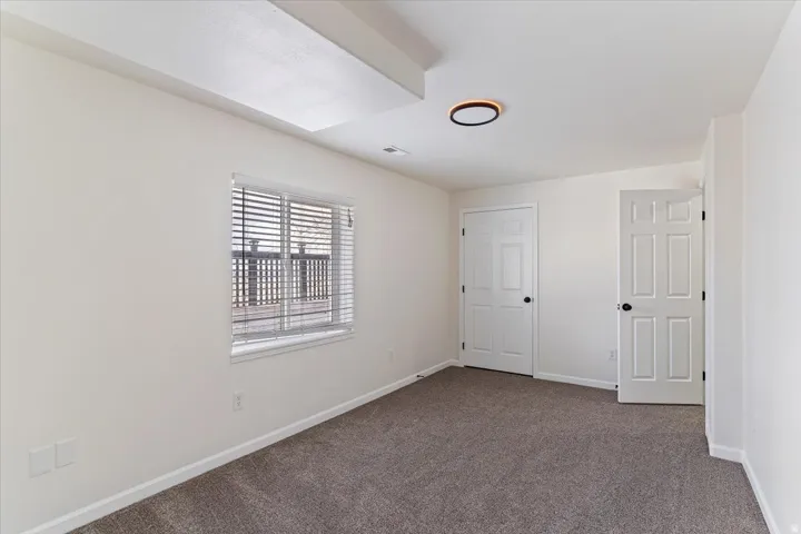 Interior room featuring neutral wall finishes, grey carpet flooring, and a large window with horizontal blinds