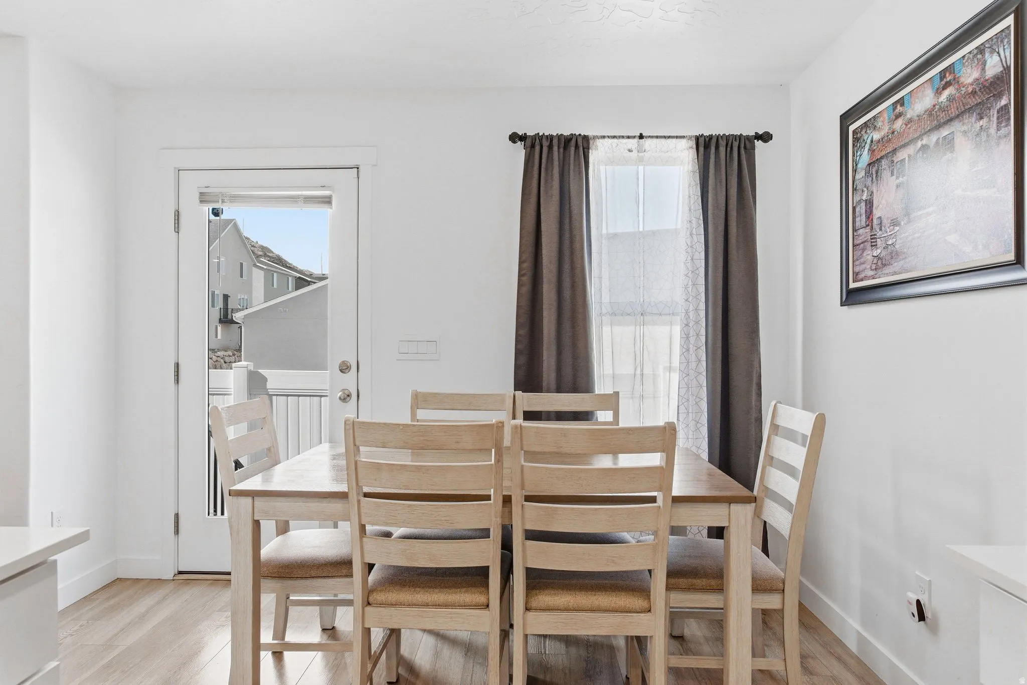 Dining area featuring wood-finish flooring, a white door leading to an outdoor space, and a window with dark curtains