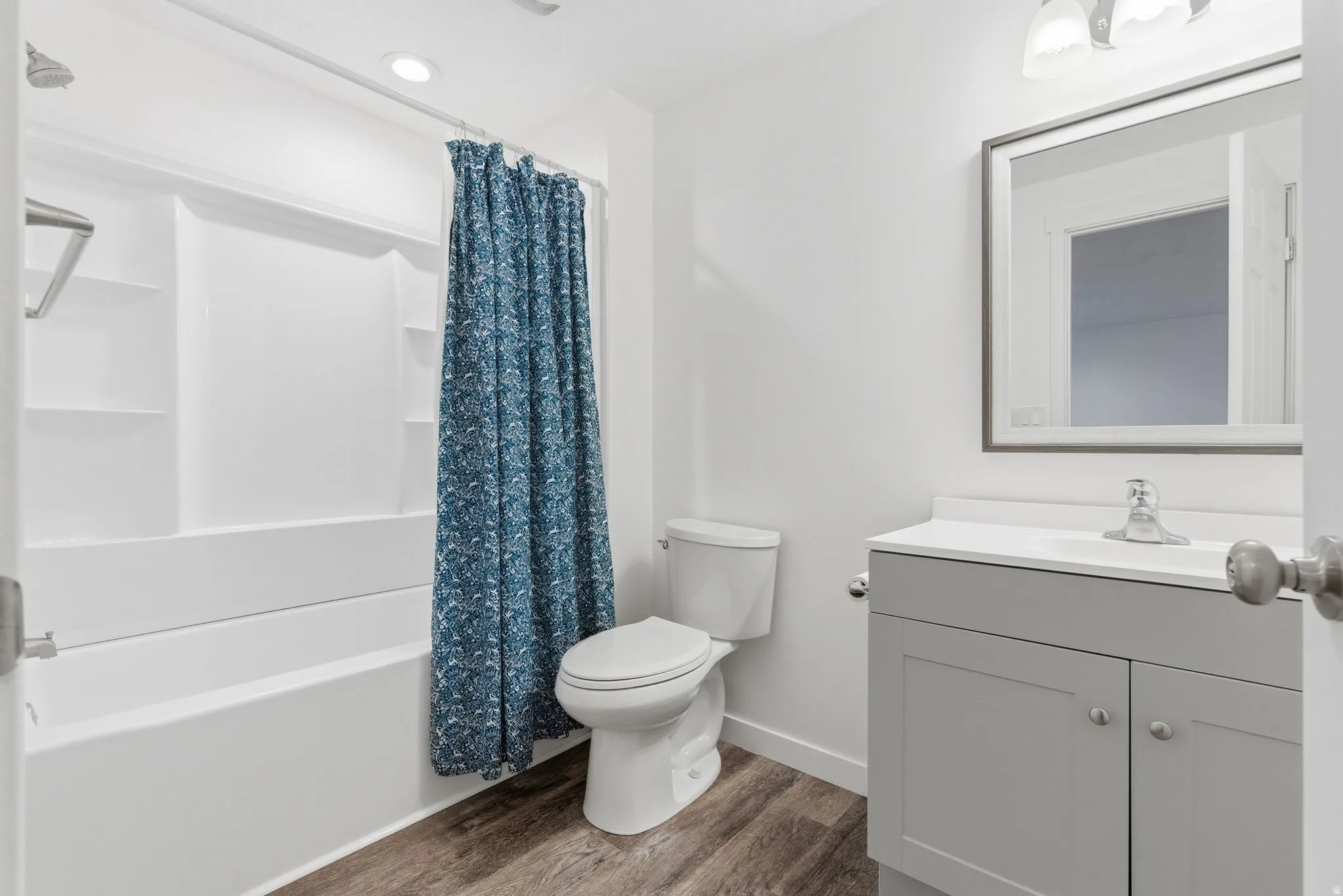 Bathroom featuring a white tub/shower combination with built-in shelving, a modern toilet, a gray vanity with a white countertop, and a framed mirror