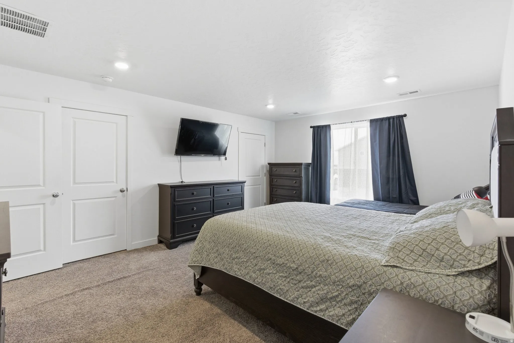 Carpeted bedroom featuring white walls, recessed lighting, and a window with sheer and blackout curtains