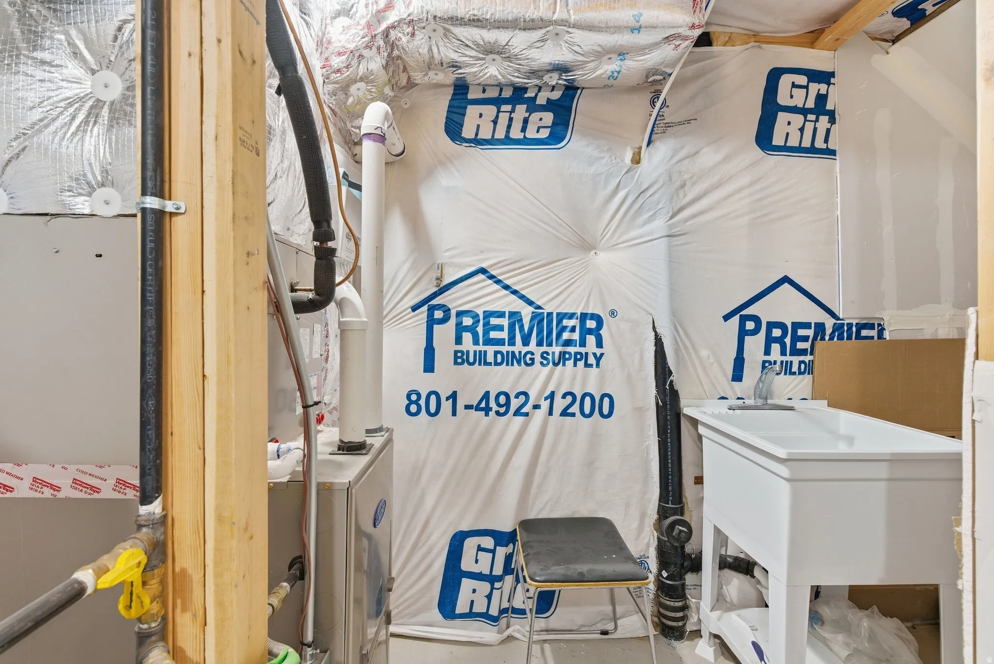 Utility area featuring a white utility sink, exposed wood framing, and visible plumbing and HVAC components