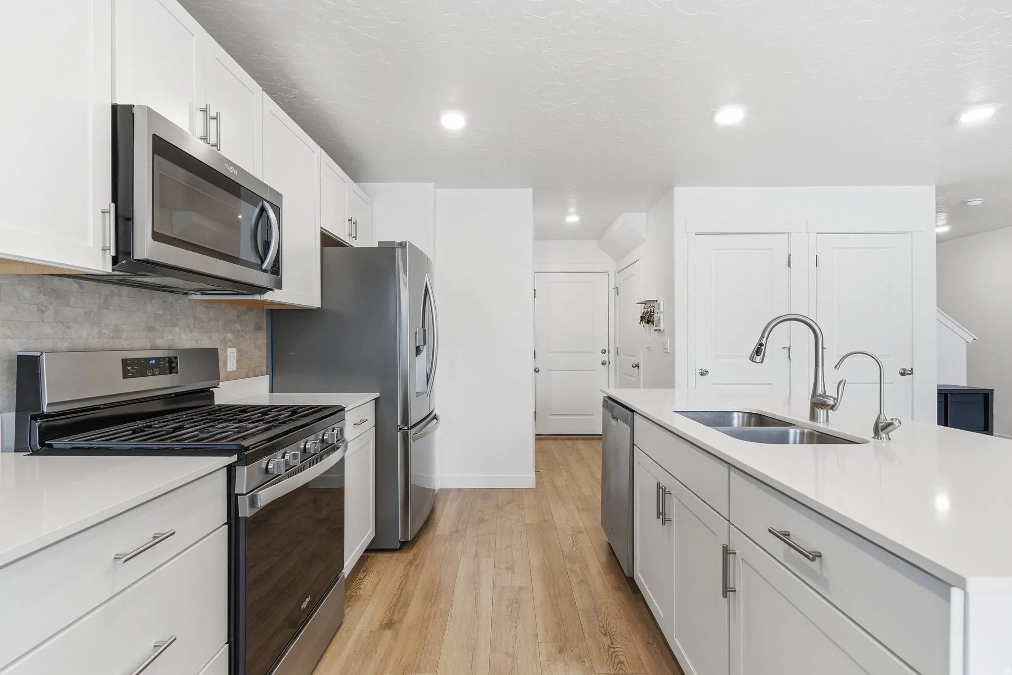Contemporary kitchen featuring white cabinetry, stainless steel appliances, light countertops, wood-finish flooring, and recessed lighting