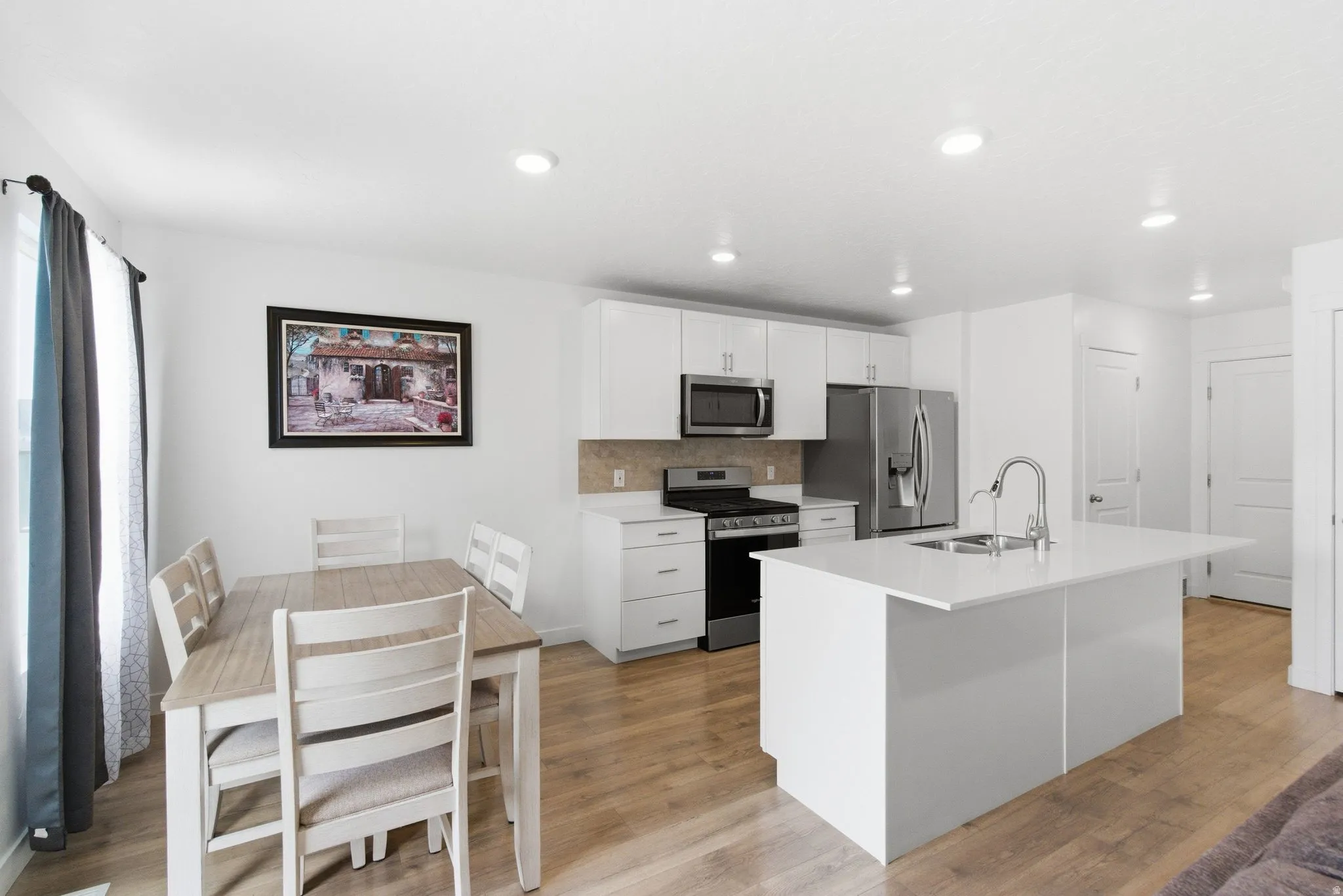 Kitchen and dining area featuring white cabinetry, stainless steel appliances, a center island with sink, recessed lighting, and wood-finish flooring