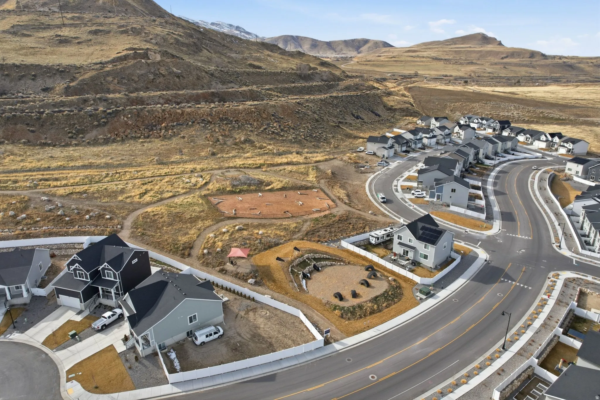 Modern residential development featuring a paved road network, uniform home designs with dark roofs, and surrounding natural terrain