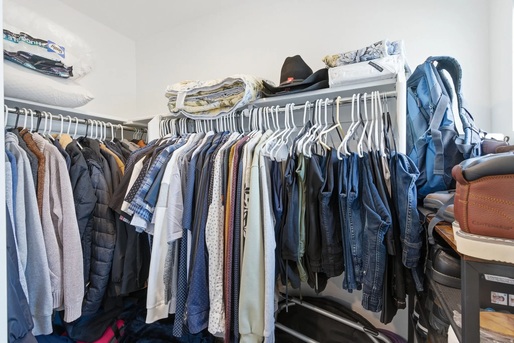 Walk-in closet with white walls, L-shaped hanging rods, and integrated shelving