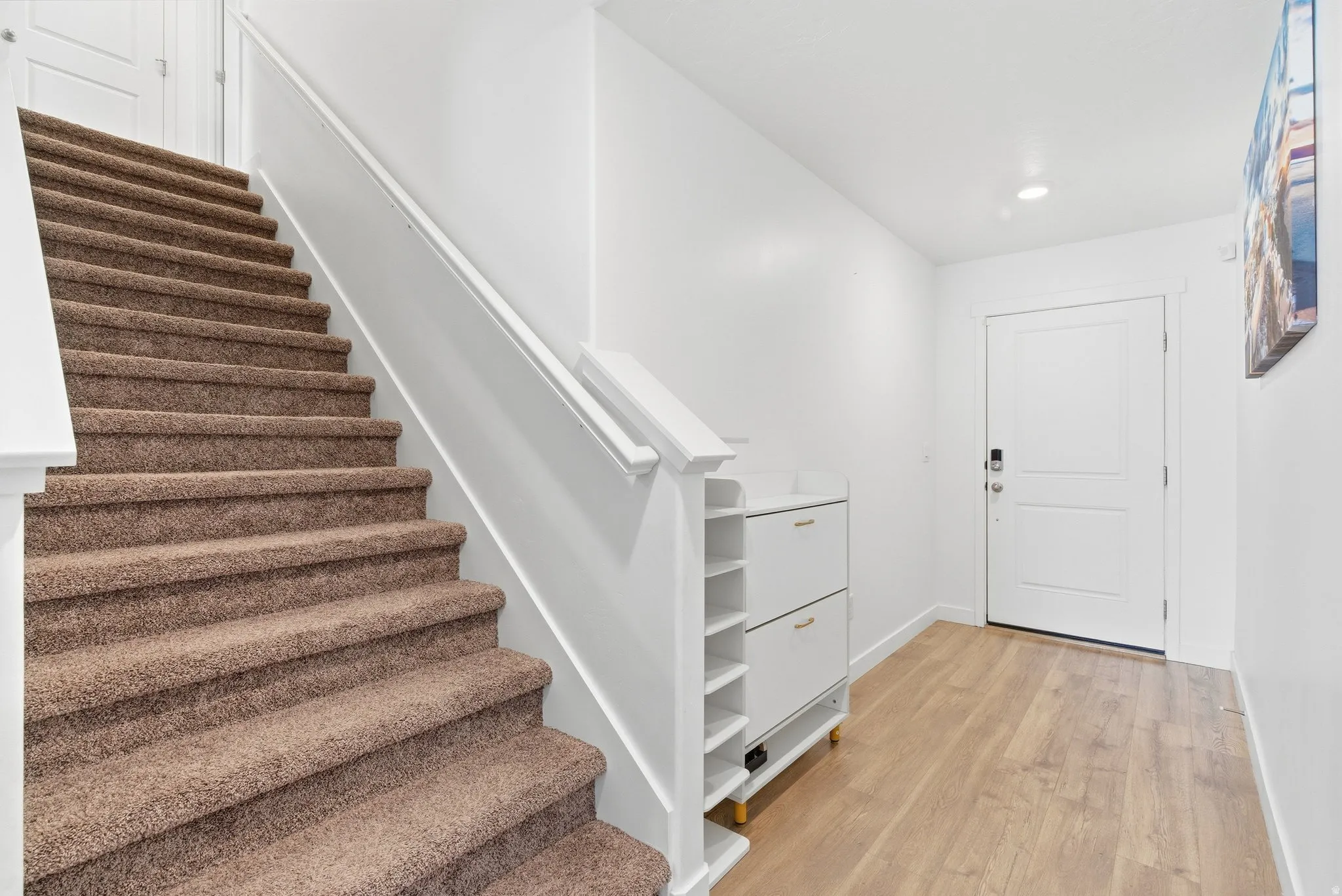Entryway featuring light wood-finish flooring, a contemporary white door with smart lock hardware, and a staircase with brown carpeting