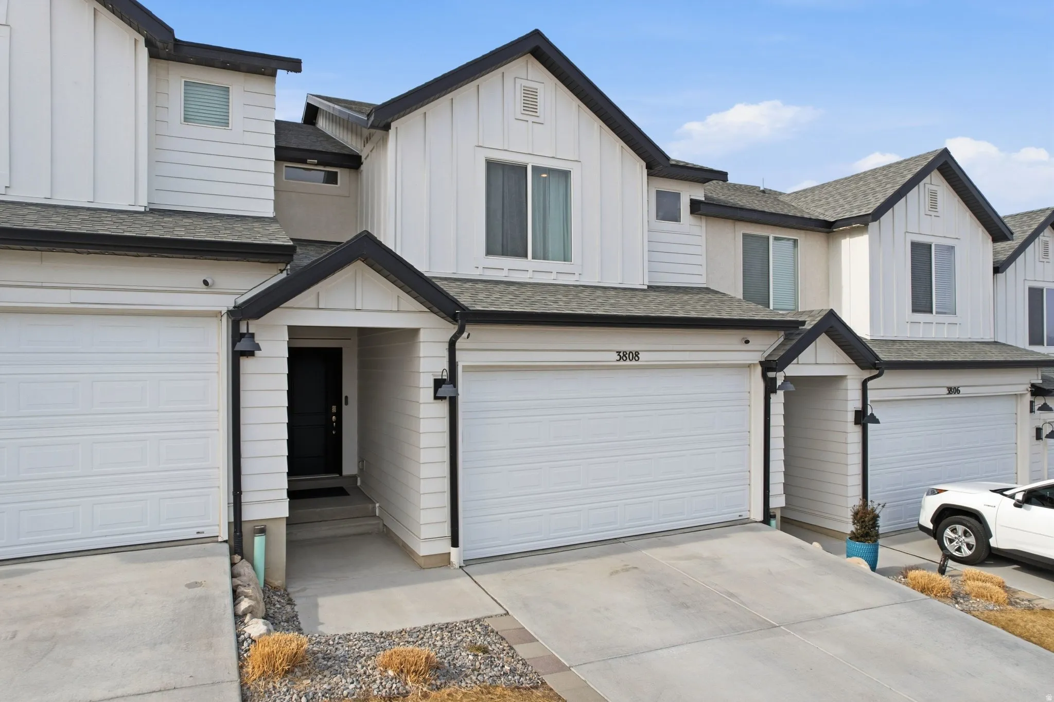 Modern townhome exterior featuring white vertical and horizontal siding, a prominent attached garage, and a covered entry with a dark door