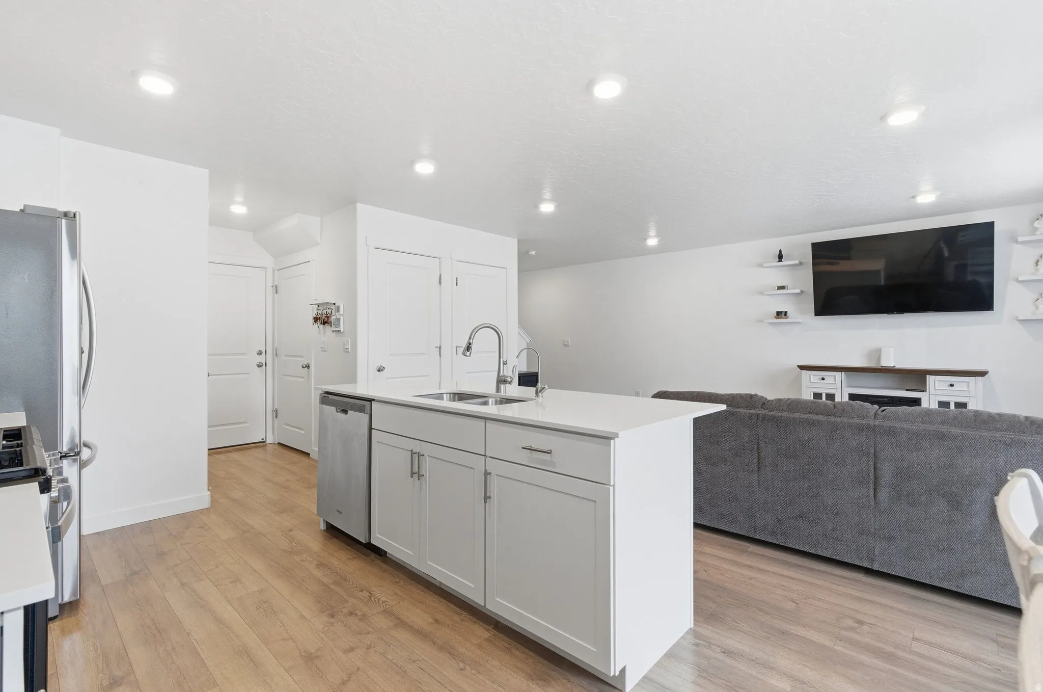 Open-concept kitchen featuring a center island with sink and integrated dishwasher, recessed lighting, wood-finish flooring, and white cabinetry