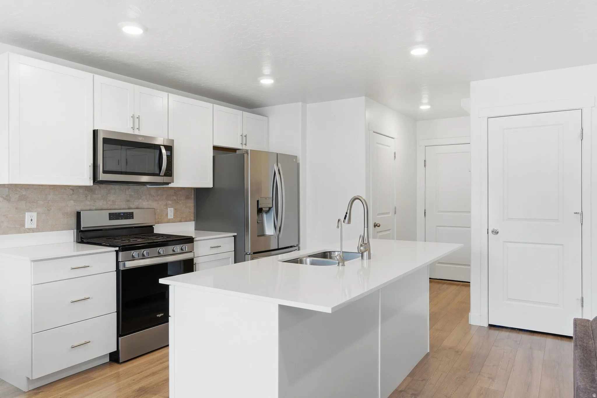Modern kitchen featuring a large island with an undermount sink, white cabinetry, stainless steel appliances, and wood-finish flooring