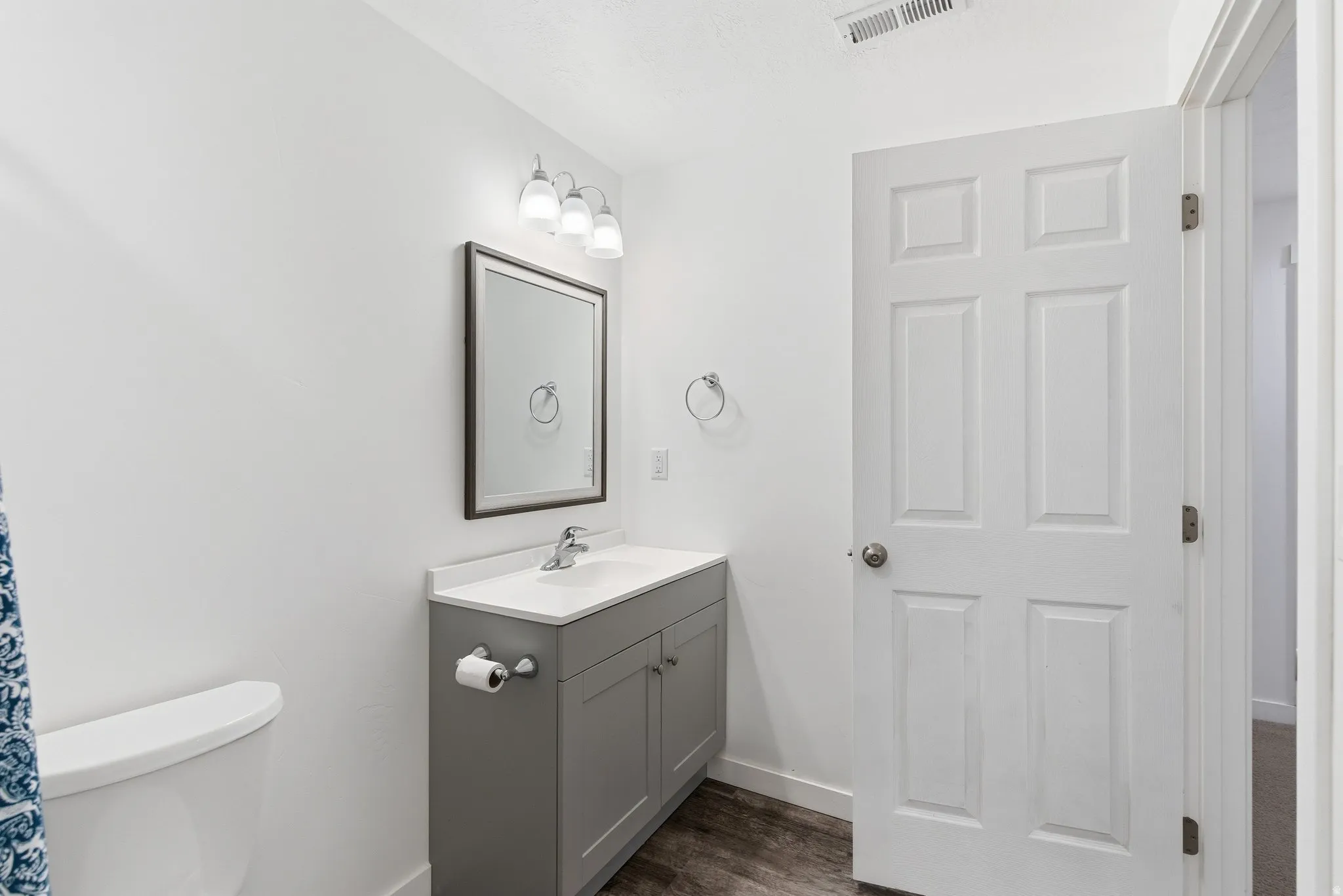 Bathroom featuring a gray vanity with a white countertop and integrated sink, a framed rectangular mirror, and overhead tri-bulb vanity lighting