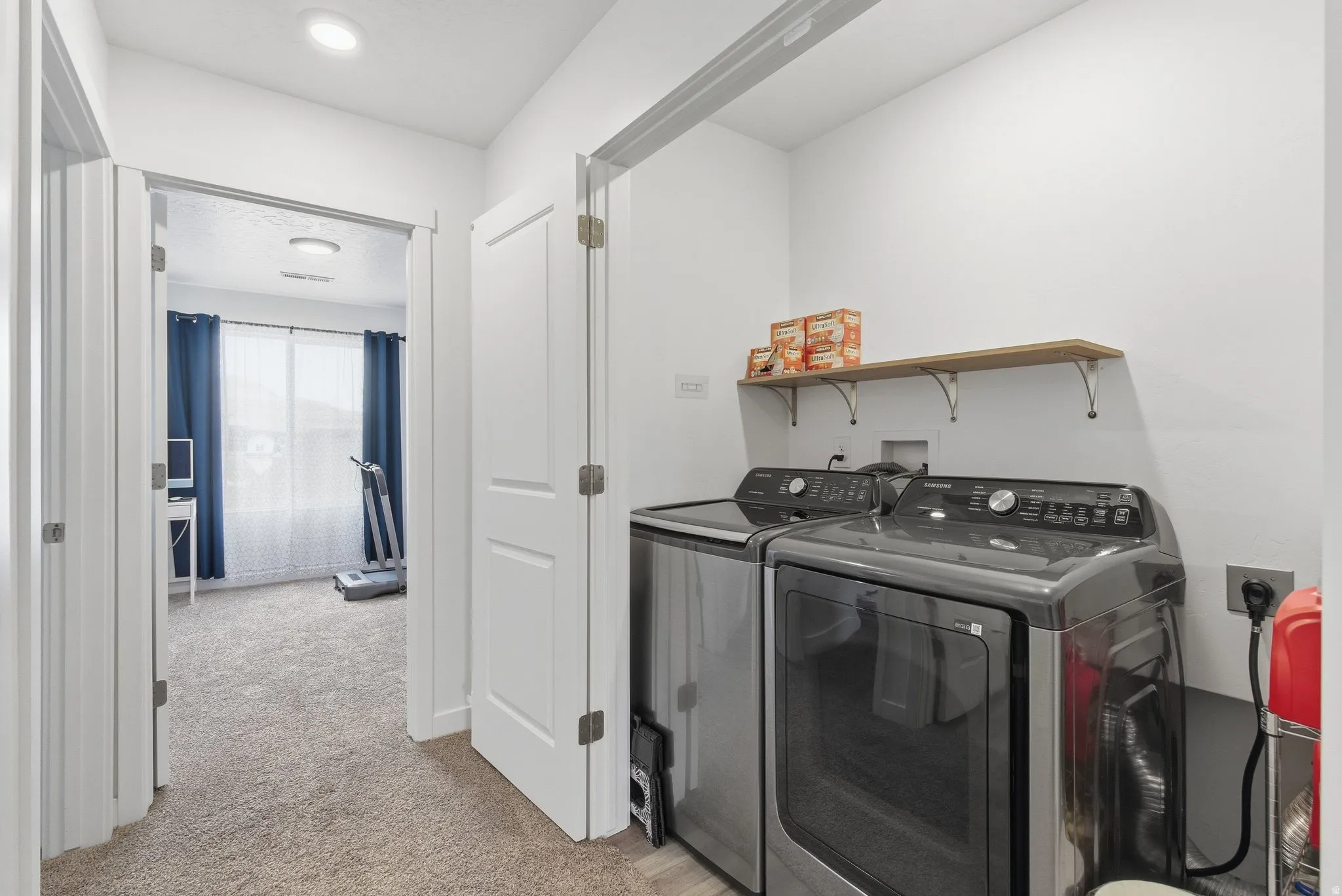 Dedicated laundry area featuring a light wood shelf with decorative brackets, and contemporary white walls