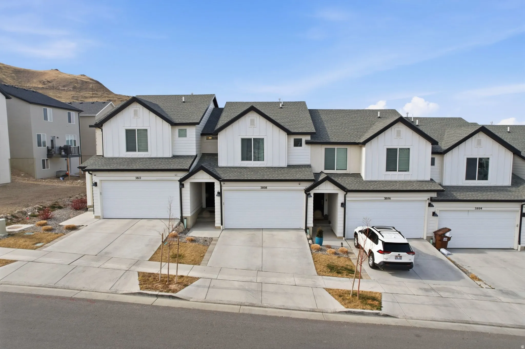 Contemporary townhome featuring a white vertical siding facade, dark trim accents, and a dark shingle roof
