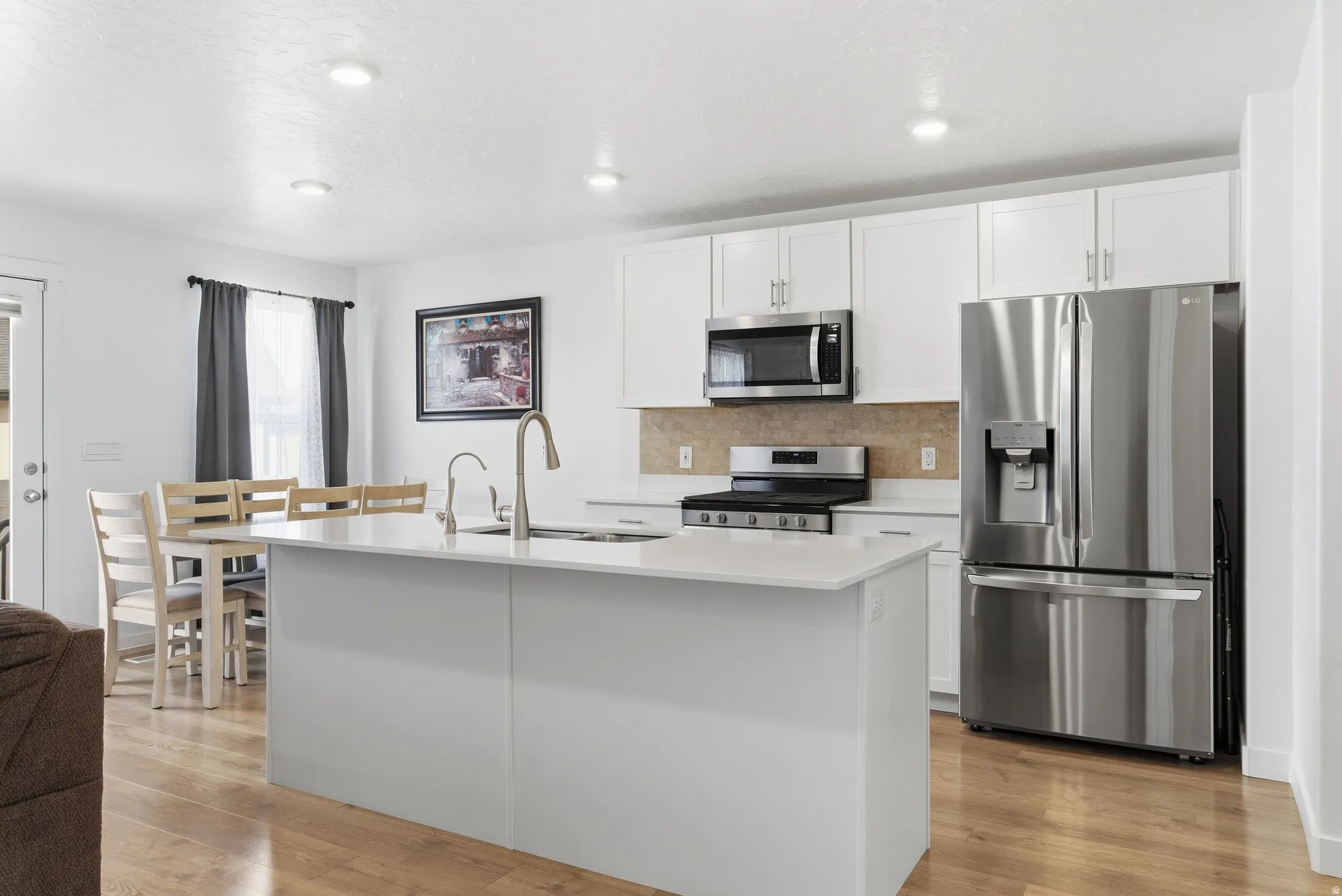 Contemporary kitchen featuring white cabinetry, stainless steel appliances, a center island with sink, wood-finish flooring, and recessed lighting